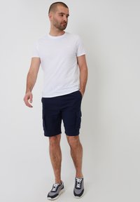 T-shirt en coton blanc associé à un short cargo bleu marine avec deux poches latérales, et des baskets grises et blanches au design sportif.