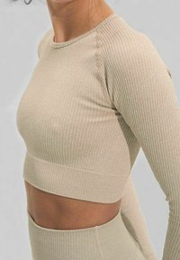 Top corto de manga larga acanalado en beige, con escote redondo y diseño ajustado. La tela tiene una textura sutil con algo de elasticidad.