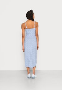 Vestido maxi floral azul com alças finas, corpete ajustado e saia fluida. Usado com ténis azul claro com solas transparentes.