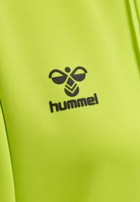 Heldere groene sportkledingstof met een zwart Hummel-logo. Het ontwerp heeft een soepele textuur met een duidelijk bij-embleem boven de merknaam.