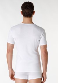 T-shirt bianca in cotone con maniche corte, design aderente, collo a giro, texture liscia e bordi a contrasto sulle maniche. Vista dalla schiena.