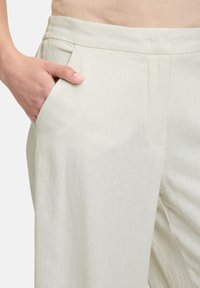 Crème-kleurige broek met wijde pijpen, een gladde textuur, een voorzak en nette plooien bij de taille. Casual fit.