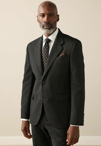 Black tailored suit with a notch lapel, white dress shirt, and patterned tie. Pocket square in burgundy adds detail. Smooth fabric finish.