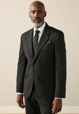 Black tailored suit with a notch lapel, white dress shirt, and patterned tie. Pocket square in burgundy adds detail. Smooth fabric finish.