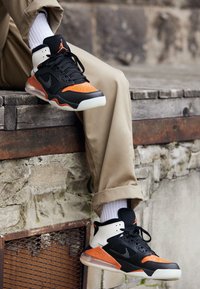 Černé a oranžové vysoké tenisky s síťovaným designem, polstrovaným límcem, gumovou podešví a průhlednými akcenty na podrážce.