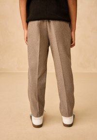 Brown checkered trousers in a relaxed fit with visible pleats, paired with white sneakers featuring black and brown accents.
