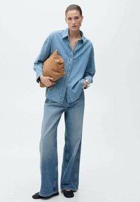 Hellblaues Jeanshemd und weit geschnittene Jeans, kombiniert mit einer braunen strukturierten Clutch. Einfaches Design mit lockerer Passform und Knopfleiste.