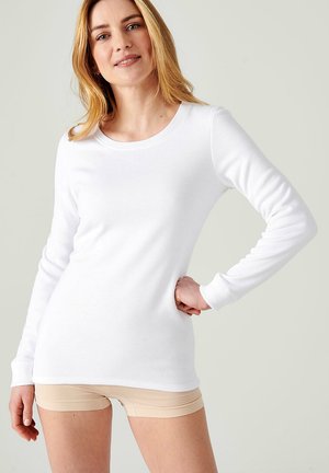 Blusa de manga larga blanca hecha de una mezcla de algodón, con cuello redondo y un diseño ajustado, combinada con pantalones cortos de color nude.