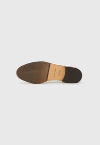 Semelle de chaussure en cuir, présentant une finition marron lisse avec un motif côtelé horizontal. La semelle intérieure est beige avec des détails de marque imprimés.