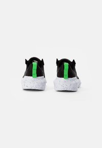 Black sneakers with thick white speckled soles and bright green pull tabs viewed from the back on a white background.
