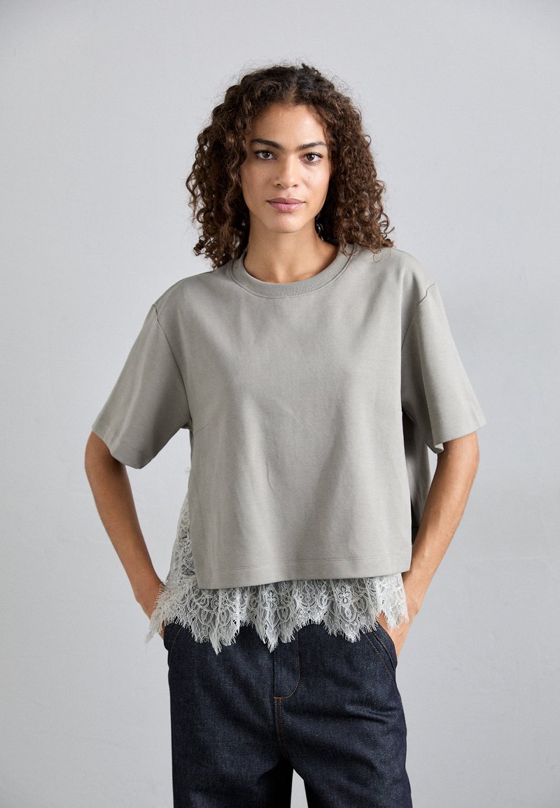 Γκρι κοντομάνικο μπλουζάκι με χαλαρή εφαρμογή και λεπτο�μέρεια από δαντέλα στο στρίφωμα, σε συνδυασμό με σκούρα τζιν παντελόνια. Υφασμάτινη επιφάνεια με ομαλή υφή.