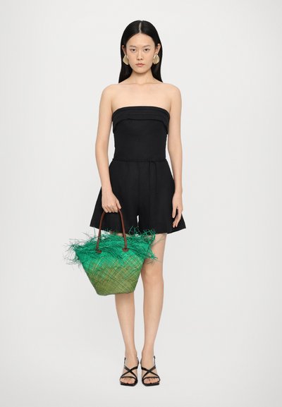 Svart strapless jumpsuit med inriktad midja, tillsammans med en grön vävd väska med fransdetaljer och bruna handtag. Svarta sandaletter med remmar.