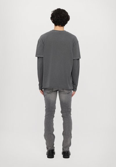 T-shirt gris oversize à manches courtes superposé à un haut à manches longues, associé à un jean skinny gris délavé et des bottes noires.