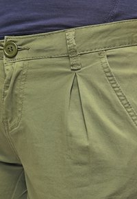 Olijfgroene katoenen shorts met een zichtbare plooi, knoopsluiting en zijzak. Gladde textuur met verstevigde stiksels.