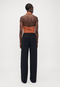 Halterneck top in roestoranje met geribbelde textuur, gecombineerd met hooggetailleerde, loszittende zwarte broek met zijzakken.