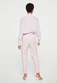 Lichtpaarse blouse met lange mouwen, gecombineerd met lichtroze tapered broek. Witte haksandalen. Glad materiaal, eenvoudig ontwerp, geen patronen.