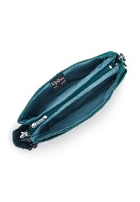 Teal stofpung med to lynlåslommer, indvendigt foret med en lysere teal, med en pelsagtig pom-pom detaljer og mærkeetiket.