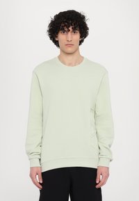Felpa verde chiaro con colletto a girocollo e maniche lunghe, caratterizzata da dettagli testurizzati sul lato inferiore destro. Realizzata in materiale morbido.