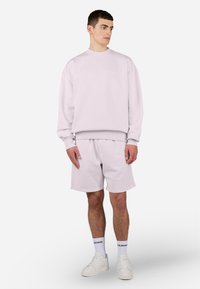 Light purple sweatshirt with long sleeves and crew neckline, paired with matching light purple shorts. White sneakers and socks with black text.