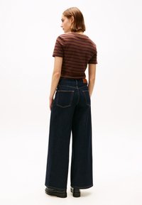 Gestreepte korte mouwen shirt in bordeaux en bruin, gecombineerd met wijdvallende donkerdenim jeans. Opvallende kenmerken zijn de achterzakken en een contrasterende tailleband.