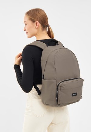 Sac à dos kaki avec des bretelles rembourrées, un haut arrondi, une poche zippée à l'avant et un label de logo. Fabriqué en matériau durable avec une texture lisse.
