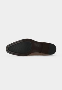 Semelle d'une chaussure habillée en cuir marron avec des patins en caoutchouc noir antidérapants au talon et à l'avant, présentée sur un fond uni.