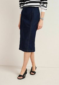 Gonna a matita in denim blu scuro con cuciture gialle a contrasto, lunghezza al ginocchio e leggermente elasticizzata. Abbinata a décolleté nere con tacco a blocco e punta aperta.