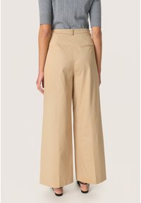 Pantaloni bej cu croi larg, cu o textură netedă, talie înaltă și un singur buzunar posterior. Asortați cu un top gri ajustat, cu dungi.