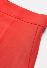 Gros plan d'un tissu rouge à texture lisse avec un ourlet cousu et un détail de couture verticale sur un vêtement.
