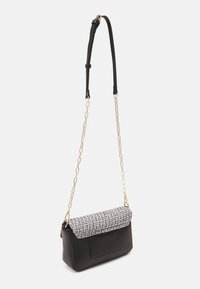 Sac d'épaule rectangulaire noir avec rabat en tweed et bandoulière en chaîne dorée avec une section ajustable en cuir noir.