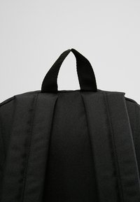 Zaino nero con spallacci imbottiti, manico superiore e tessuto testurizzato. Design minimalista senza loghi o motivi visibili.