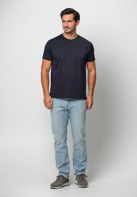 Sjöblå kortärmad t-shirt med rund halsringning, kombinerat med ljusblå jeans och grå sportskor. Enkel design, mjukt bomullsmaterial.