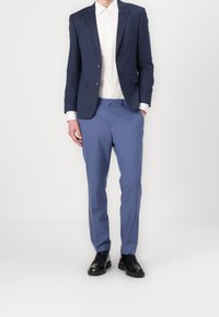 Marineblauer Textur-Blazer über einem weißen Hemd, kombiniert mit hellblauen Hosen und schwarzen Schuhen. Maßgeschneiderte Passform mit dezenten Akzenten auf dem Jacket.