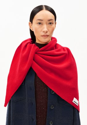 Rode wollen sjaal om de schouders gewikkeld, met een gladde textuur. Dragen over een donkerblauwe jas met knoopdetails en een geribde bruine trui.