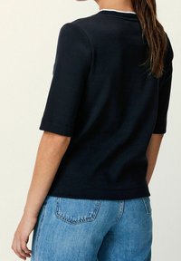 Black short-sleeve top with a crew neck, featuring a smooth texture and a clean design. Paired with light blue denim jeans.