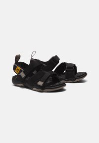 Sandálias pretas com tiras ajustáveis, solas de borracha texturizadas e palmilha almofadada. Apresenta uma etiqueta com um logótipo perto do calcanhar.