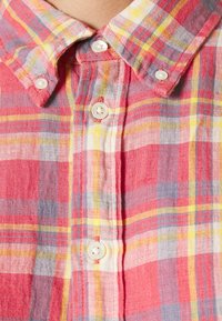 Detailní záběr na červenou, žlutou a fialovou kostičkovanou košili s knoflíky v bílé barvě a složeným límcem.