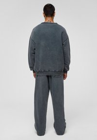 Grijze oversized sweatshirt en bijpassende wijde broek van zachte stof. Heeft stiksel-details en een losvallende pasvorm voor comfort.