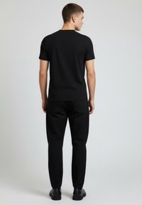 Czarny t-shirt z krótkim rękawem i okrągłym dekoltem, połączony z czarnymi spodniami. Gładka faktura, dopasowany krój i minimalistyczny styl.