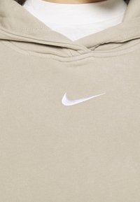 Beige hoodie made of soft fabric featuring a front pocket, drawstring hood, and small white Nike logo on the chest.