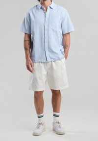 Košile s krátkými rukávy v světle modré barvě s bílými pruhy, doplněná o bílé šortky. Disponuje náprsní kapsou a volným střihem.