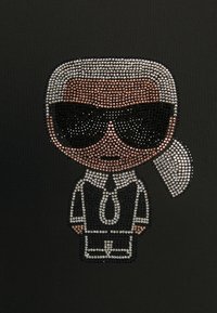 Svart bakgrund med en kristallbesatt tecknad figur som har solglasögon, vit krage och slips. Silver-, svart- och kopparaccent.