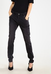 Černé džíny z denimu s úzkým střihem, obsahující dekorativní cvočky podél předních kapes, pět kapsový design a světlé vyblednutí.