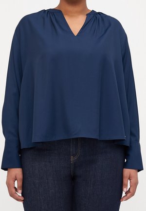 Marineblå langærmet bluse med V-hals, rynkedetaljer ved skuldrene og en løs, flydende pasform. Glat stoftekstur.