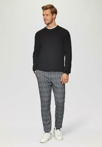 Schwarzer strukturierter Pullover, karierte Hose in Blau und Grau, und weiße Sneaker. Mit rundem Ausschnitt und taillierter Passform.