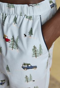 Gaiši zili pidžamas šorti ar atkārtotu sarkano un zilo kravas automašīnu, zaļo koku un suņa rakstu. Iezīmē mīkstu tekstūru un elastīgu jostu.