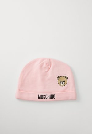 Gorro de bebé rosa claro com aba dobrada, texto preto "MOSCHINO" e um pequeno gráfico da cara de um ursinho do lado.