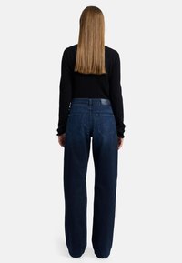 Jeans a gamba larga blu scuro con una vita alta, dotati di tasche posteriori e una texture di tessuto piatto, abbinati a un top nero a maniche lunghe.