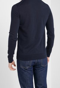 Navyblå långärmad tröja med ribbade mudd och nederkant, tillverkad av mjukt material; sedd från baksidan, tillsammans med mörka denimjeans.