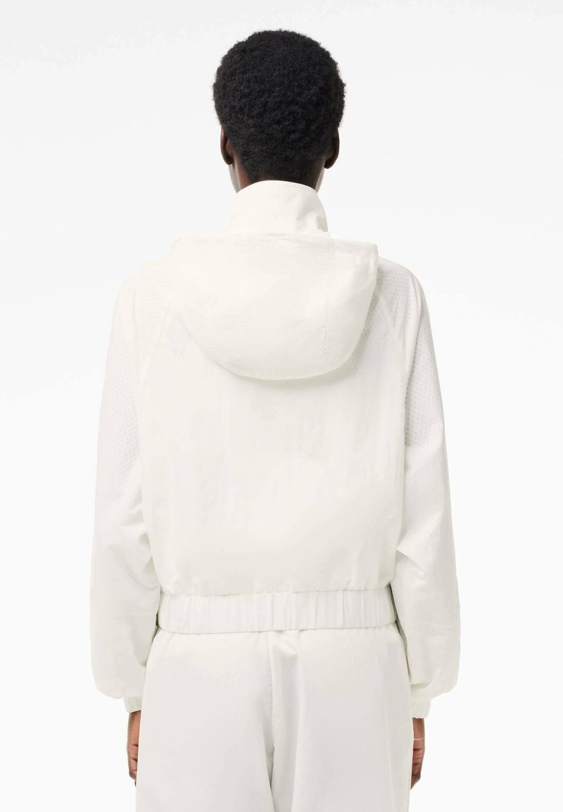 Biała kurtka z kapturem o teksturowanej tkaninie, elastycznym pasie i mankietach. Posiada gładkie wykończenie i minimalistyczny design.